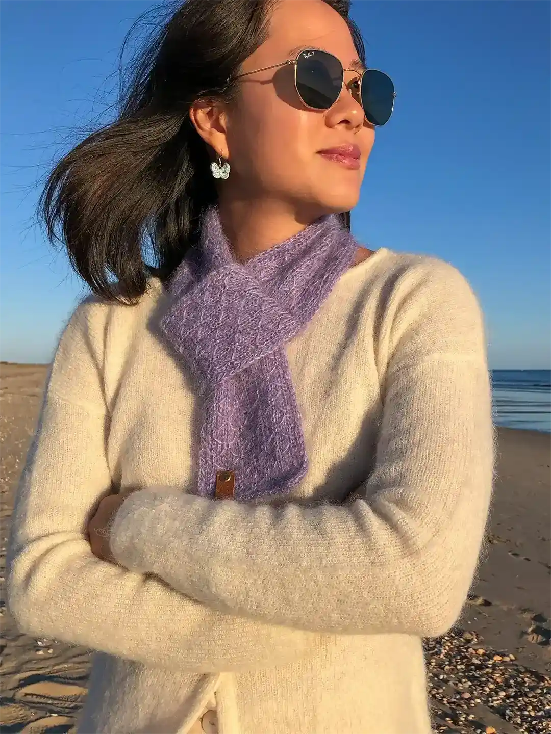woman wearing lilac hand knitted wool scarf with trellis pattern on a beach in vila real de santo antonio algarve